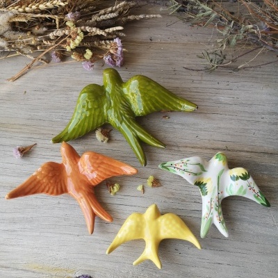 Quatro pássaros decorativos em cerâmica colorida sobre fundo de madeira clara