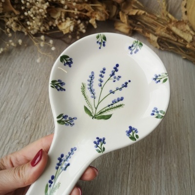 Colher cerâmica branca com padrão floral azul e verde em fundo de madeira