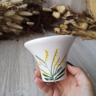 Vaso de cerâmica branco com desenho floral amarelo e verde numa mão