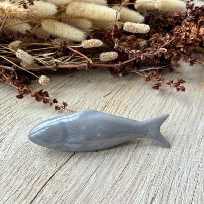 Peixe escultórico cinzento sobre madeira clara com plantas secas ao fundo