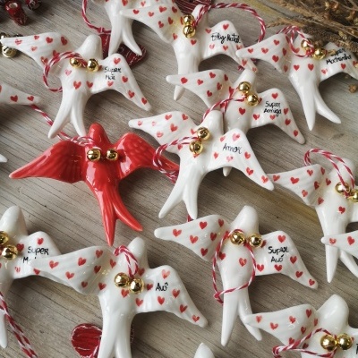 Pendentes cerâmicos em forma de pássaros brancos e vermelhos com corações vermelhos, sinos dourados e fitas para pendurar.