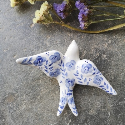 Pássaro decorativo em cerâmica branca com pintura azul e flores secas ao fundo