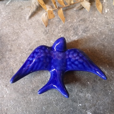 Pássaro cerâmico azul sobre superfície rugosa cinzenta com folhas secas.