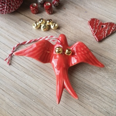Pássaro decorativo em cerâmica vermelha com sinos dourados e cordão vermelho e branco