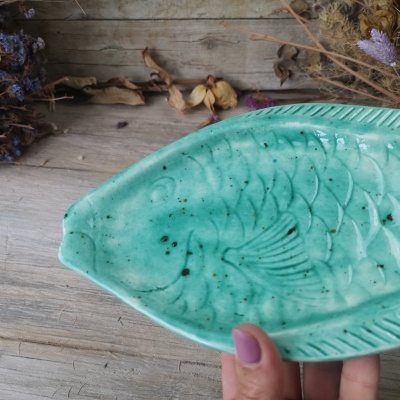 Prato decorativo em cerâmica verde turquesa em forma de peixe sobre madeira com raminhos secos