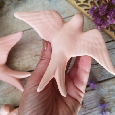 Pássaro decorativo rosa em cerâmica com textura lisa segurado pela mão