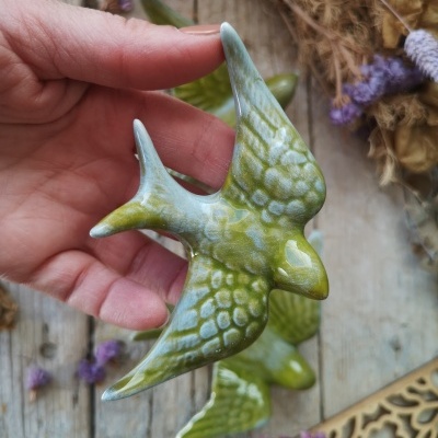 Pássaro decorativo verde de cerâmica segurado por mão