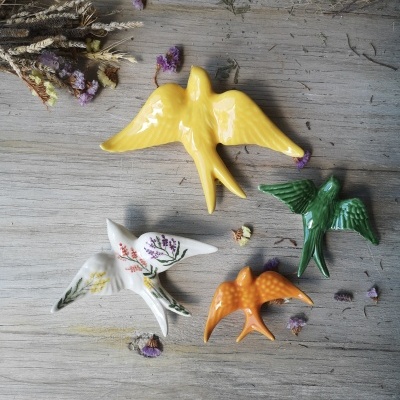 Quatro pássaros de cerâmica coloridos sobre madeira com flores secas