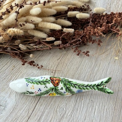Peixe decorativo em cerâmica com pintura floral colorida sobre mesa de madeira e flores secas ao fundo