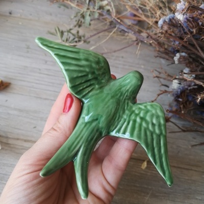 Escultura de pássaro verde de cerâmica na mão com fundo de ramos secos