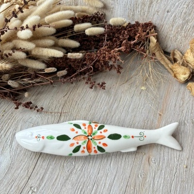 Peixe decorativo em cerâmica branca com pintura floral colorida em fundo de madeira e plantas secas