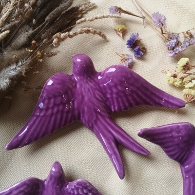 Pássaros decorativos de cerâmica roxa junto com flores secas sobre tecido beige