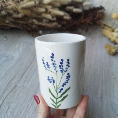 Caneca branca com desenho de flores azuis, mão com unhas vermelhas a segurá-la.