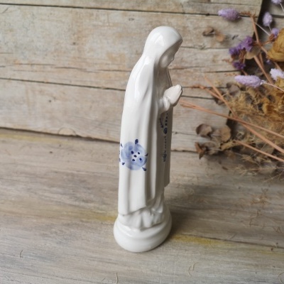 Estátua religiosa branca com detalhes azuis sobre madeira com flores secas