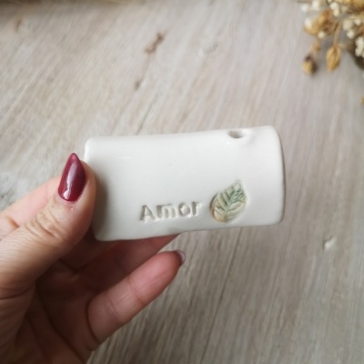 Peça de cerâmica branca com a palavra Amor e uma folha gravada