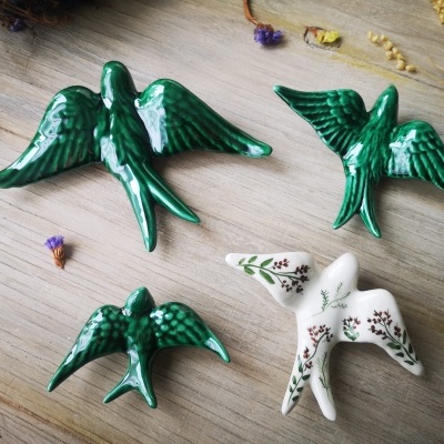 Figuras decorativas de pássaros em cerâmica verde e branca com padrão floral sobre madeira clara
