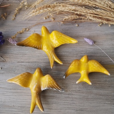 Três pássaros decorativos amarelos em cerâmica sobre madeira com ramos de trigo secos