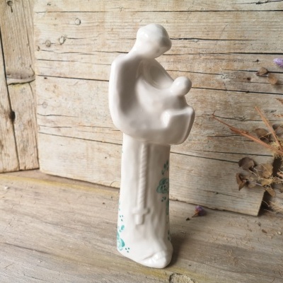 Estátua de cerâmica branca de mãe a segurar bebé em ambiente rústico