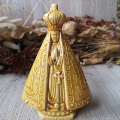 Estatueta cerâmica amarela de figura religiosa com coroa e vestido detalhado em relevo