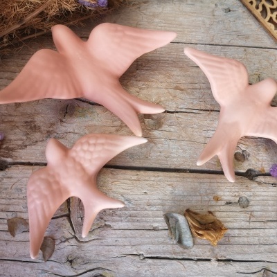 Três pássaros decorativos cor de rosa sobre madeira rústica com flores secas