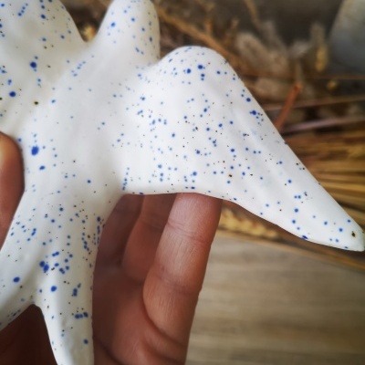 Escultura branca com manchas azuis com textura lisa sendo segurada por uma mão