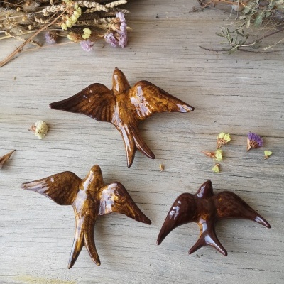 Três pássaros decorativos em cerâmica castanha sobre mesa de madeira com flores secas