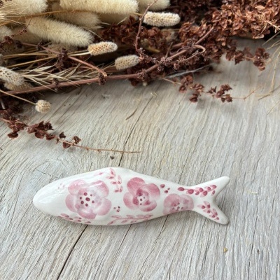 Peixe decorativo em cerâmica branca com pintura floral rosa junto a flores secas.