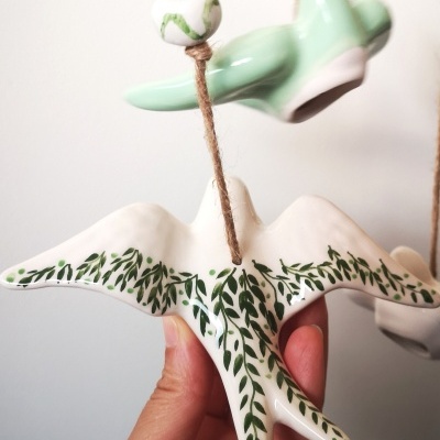 Móbile cerâmico de pássaros branco e verde com padrão de folhas pendurado em corda