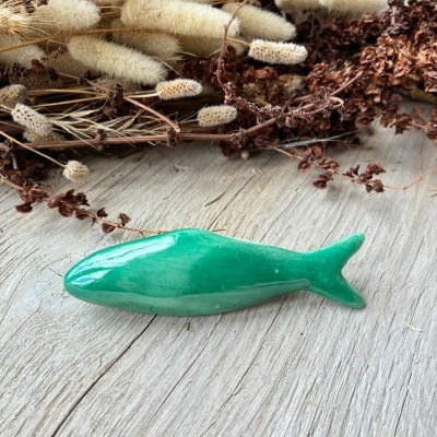 Peixe decorativo verde em cerâmica sobre madeira com flores secas ao fundo