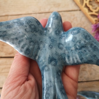 Pássaro azul decorativo com padrão de manchas segurado por mão sobre fundo de madeira