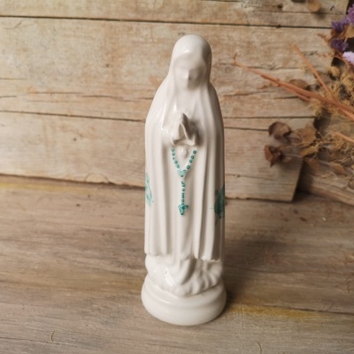 Estátua branca de Nossa Senhora com terço azul em madeira rústica