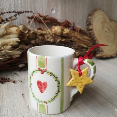 Caneca de cerâmica com padrão verde, vermelho e amarelo e ornamento de estrela amarela pendurado no cabo