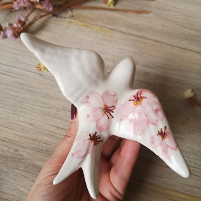 Escultura decorativa de pássaro em cerâmica com flores cor-de-rosa sobre superfície de madeira
