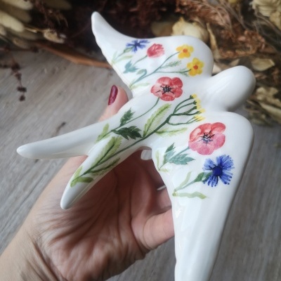 Estatueta cerâmica pássaro branco com flores pintadas coloridas e mão segurando.