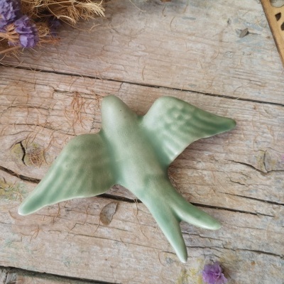 Pássaro decorativo verde em cerâmica sobre madeira rústica com flores secas roxas