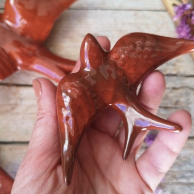 Figura decorativa de pássaro em cerâmica castanho acobreado segurada por uma mão sobre madeira