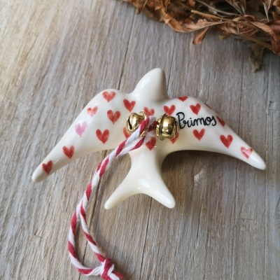 Peça decorativa branca em cerâmica em forma de pássaro com corações vermelhos e sinos dourados