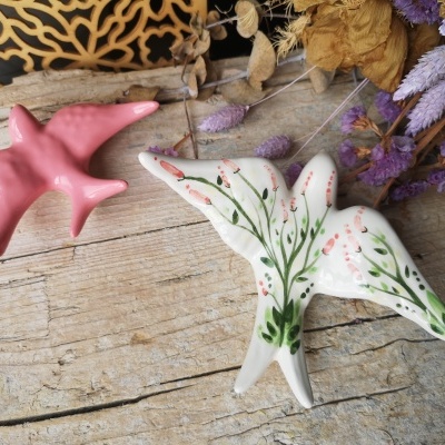 Duas figuras de pássaros em cerâmica colocadas em madeira com flores secas ao fundo