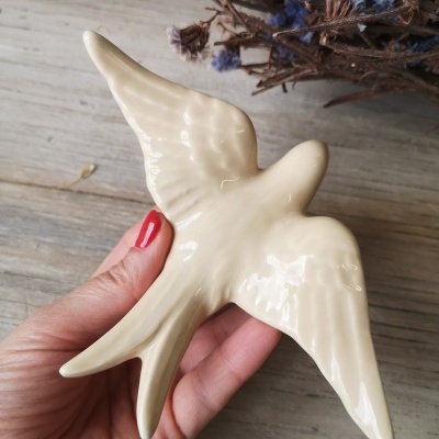 Figurinha decorativa branca em formato de pássaro segurada por mão com unhas vermelhas