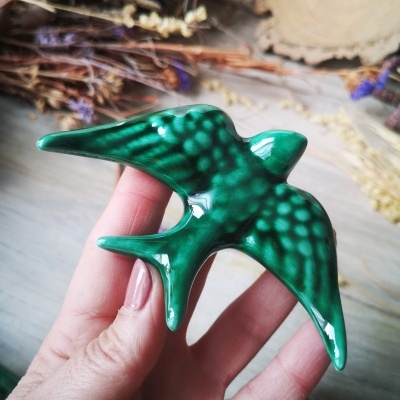 Pássaro decorativo verde em cerâmica com manchas, segurado à mão