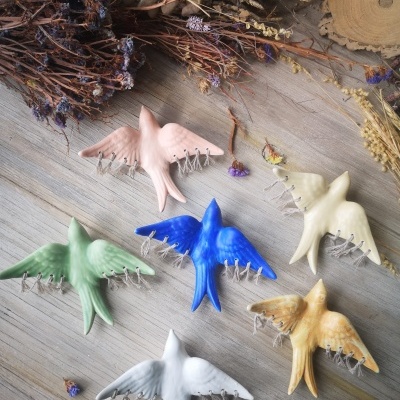 Bordados de cerâmica em forma de pássaros de várias cores numa mesa de madeira com raminhos secos