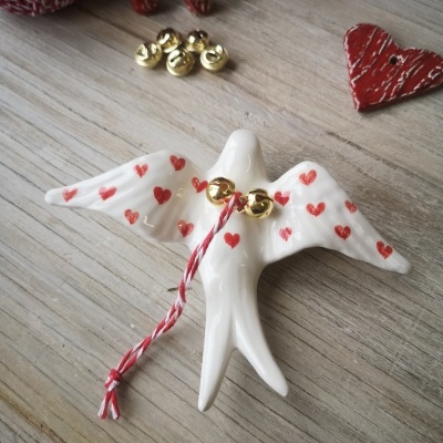 Pássaro decorativo branco com corações vermelhos e cordão com sinos dourados sobre mesa de madeira clara