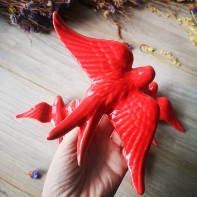 Escultura de pássaros vermelhos de cerâmica brilhante na mão com flores secas ao fundo