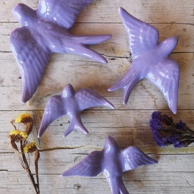 Quatro pássaros decorativos lilás em cerâmica sobre madeira clara com flores secas amarelas e roxas
