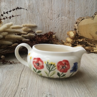 Pote de cerâmica branca com flores pintadas sobre mesa de madeira com flores secas ao fundo