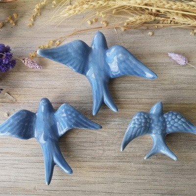 Figuras de pássaros azuis em cerâmica sobre superfície de madeira com decoração de ramos secos e flores.
