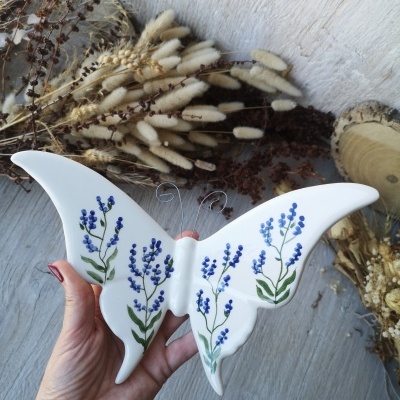 Pendurador de parede borboleta branco com flores azuis e folhas verdes em cerâmica.