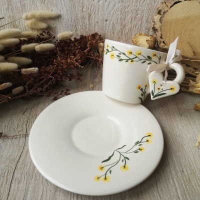 Conjunto de chávena e prato branco com flores amarelas, em fundo de madeira e ramos secos