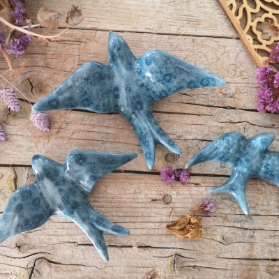 Três pássaros decorativos de cerâmica azul sobre madeira com flores secas roxas