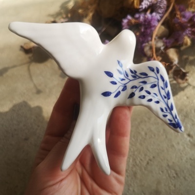 Estatueta de pássaro em cerâmica branca com folhas azuis na asa